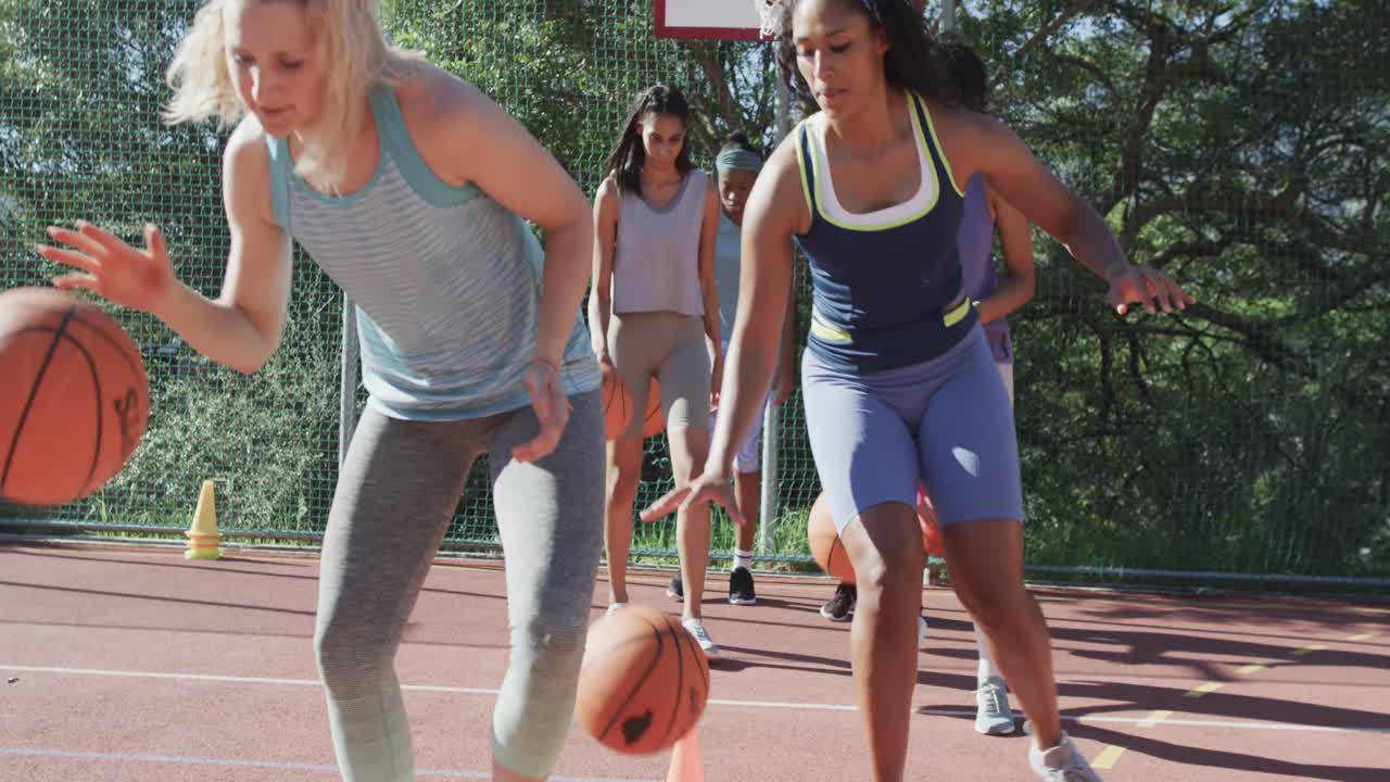 Happy diverse female basketball team training on sunny court, in slow motion