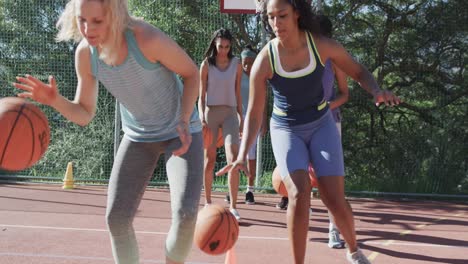 Happy-diverse-female-basketball-team-training-on-sunny-court,-in-slow-motion