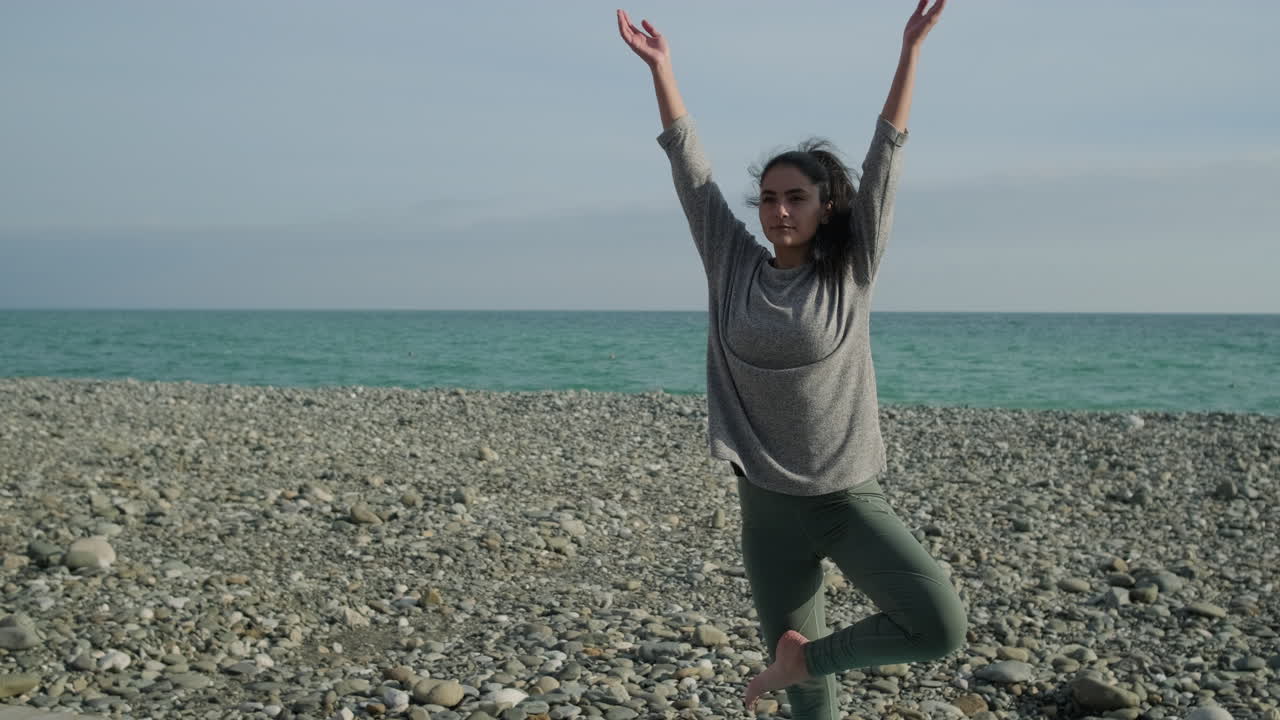 mujer practicando yoga en una playa de guijarros