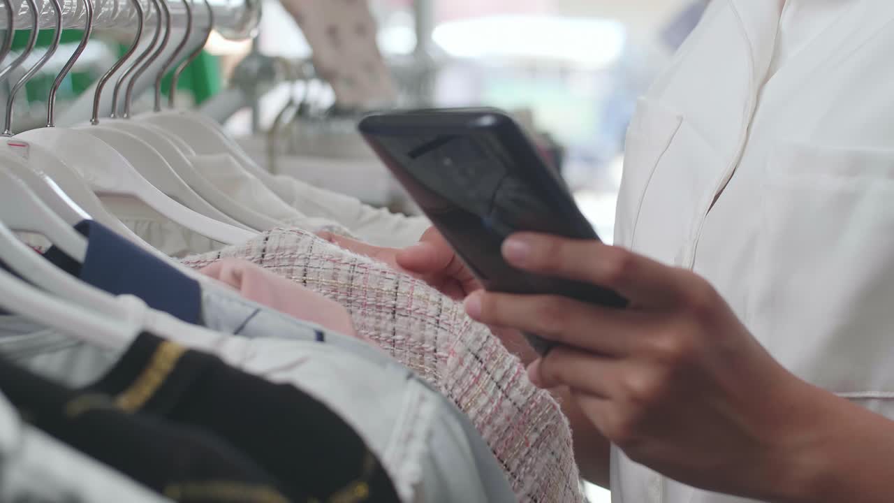소매점 에서 스마트폰 을 사용 하여 옷 을 구입 하는 여자