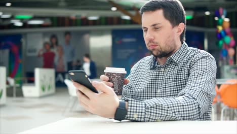 hombre bebiendo café y usando un teléfono inteligente en una cafetería