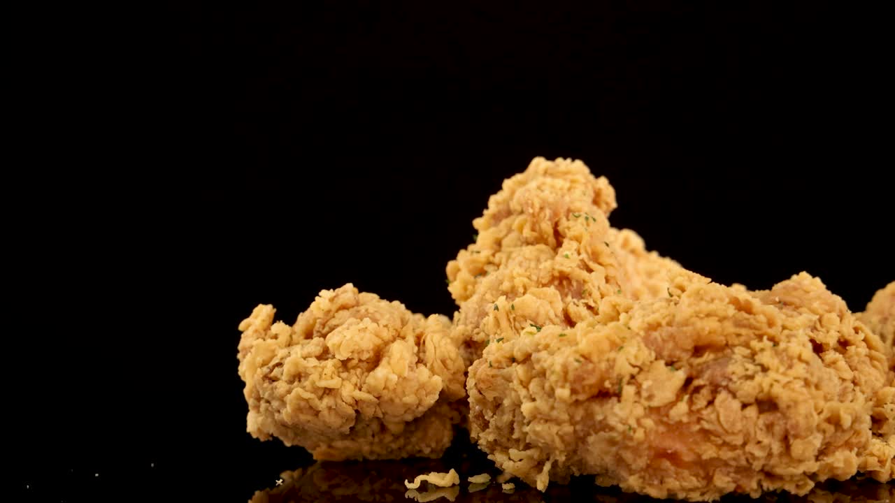 Golden, crumbed chicken breasts and thighs rotate and zoom in slow motion against a black background, highlighting crispy texture and sprinkled herbs