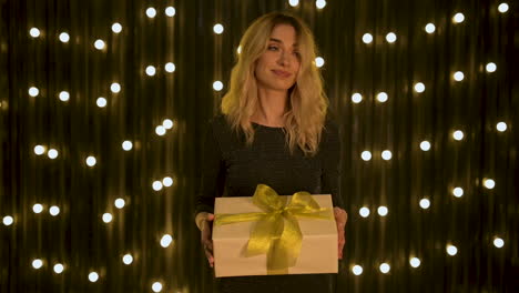 young beautiful woman holding a gift box with golden bow while falling glitter confetti