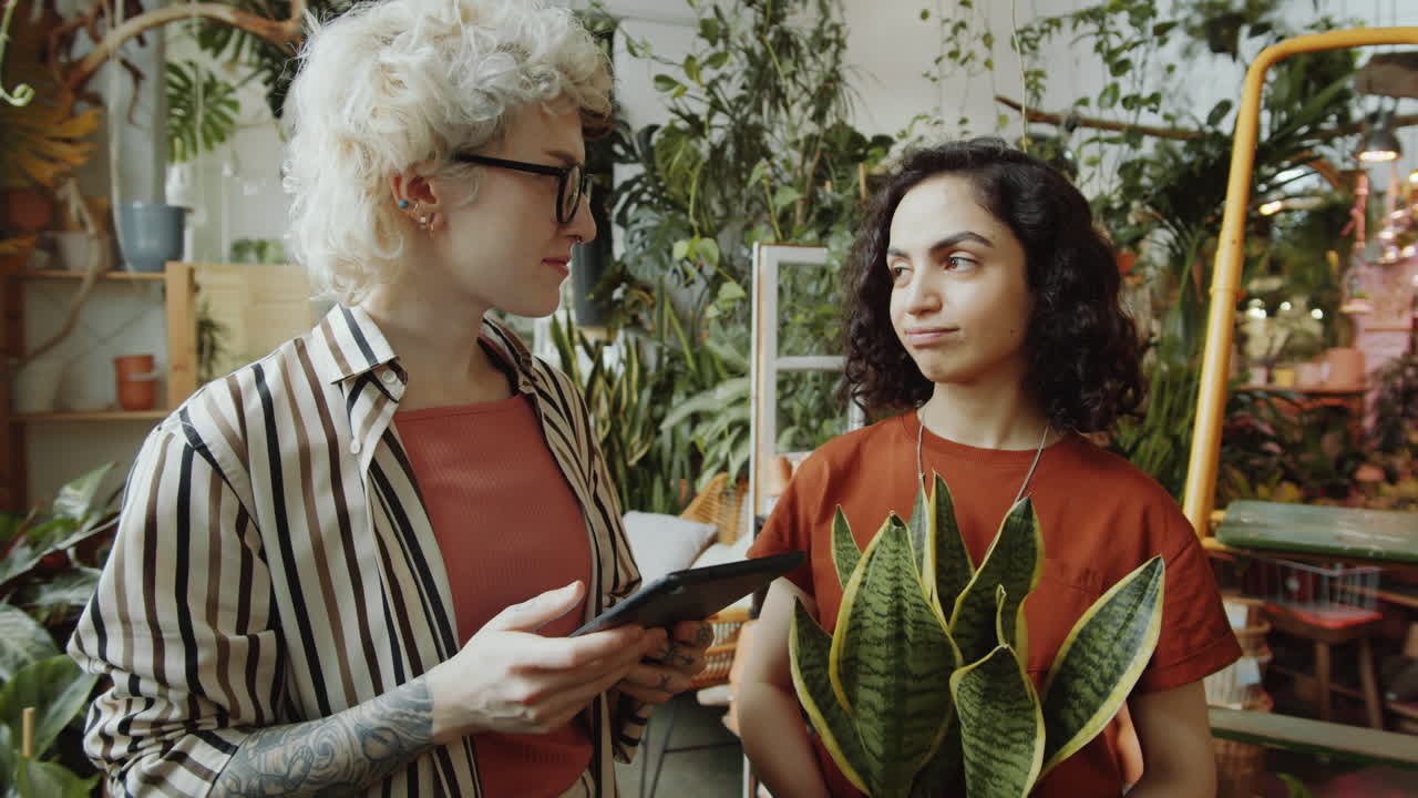jóvenes floristas usando tableta y hablando en la tienda de flores