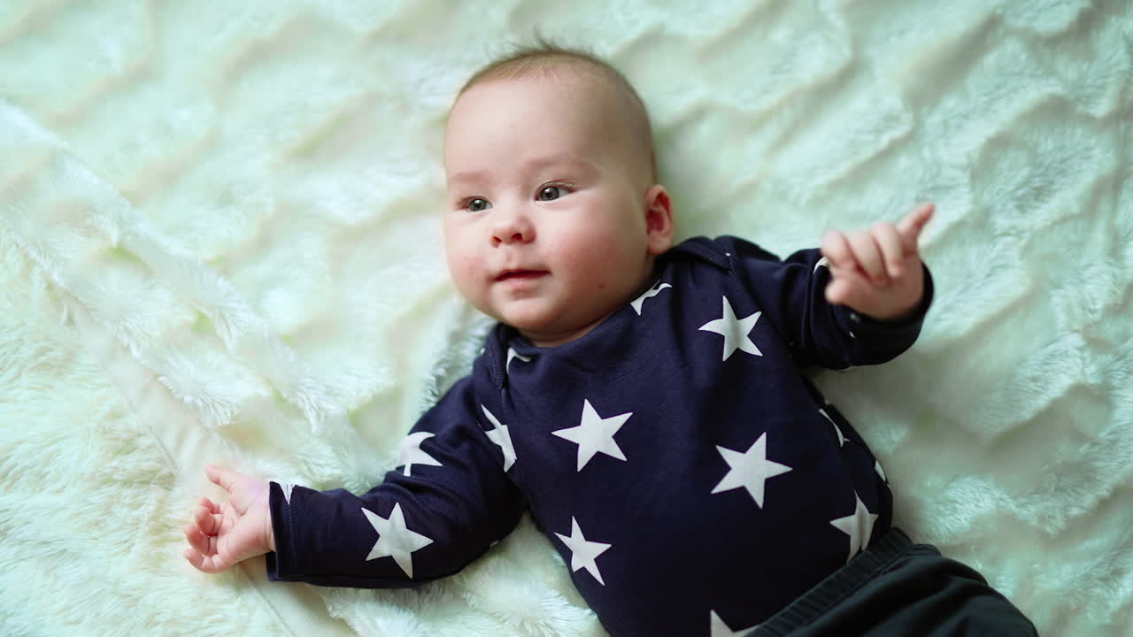 Cute Caucasian little boy lies on the soft plaid and looks at camera. Baby in blue sweater with stars at white backdrop.