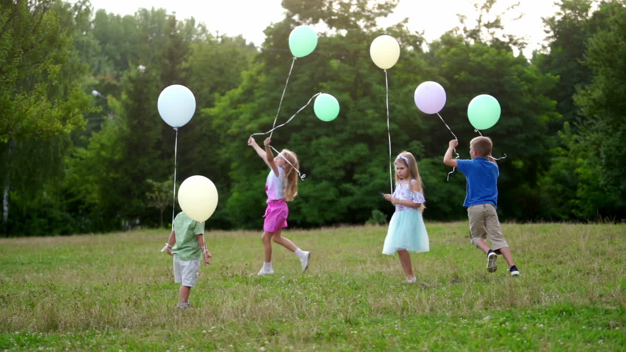 A little lovely kids outdoor with colorful baloons. Happy childen are running on the green grass with colorful balloons in her hands. The concept of freedom, a child's dream, a happy family.