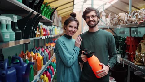 retrato de una pareja joven positiva en la tienda de jardines con un pulverizador de naranja