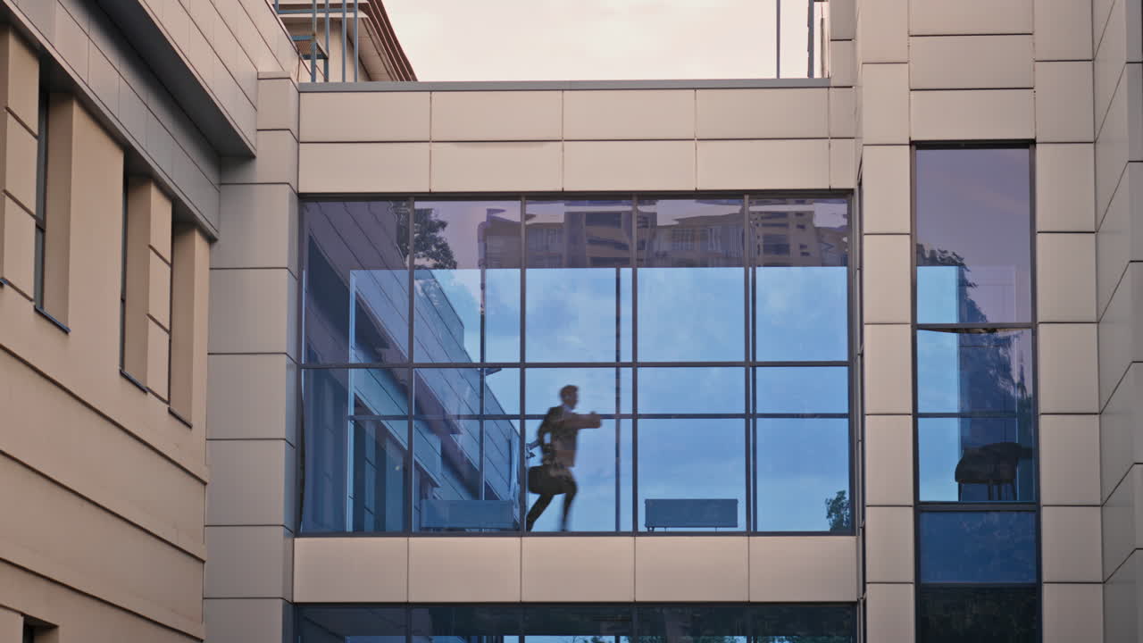 Silhouette man running inside modern glass corridor of corporate building