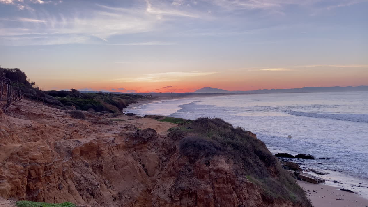 Caldo bagliore del tramonto sull'Oceano Atlantico, che lambisce le scogliere frastagliate della costa dell'Algarve e la spiaggia sabbiosa.