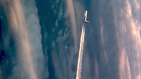 cropped portrait view from cockpit of flying airplane above clouds leaving long white condensation vapor air trail in blue sky