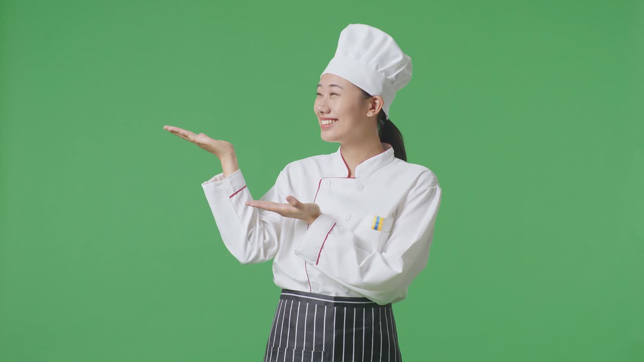 Asian Woman Chef Smiling And Pointing To Side While Standing In The Green Screen Background Studio