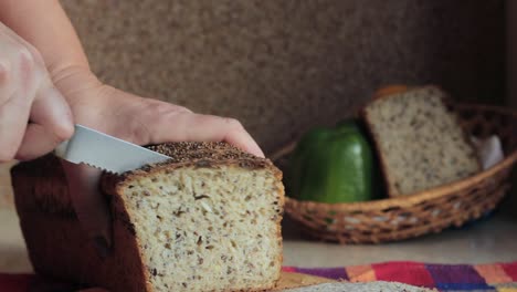 Slow-motion-close-up-shot-focusing-on-woman's-hands-using-a-bread-knife-and-slicing-a-whole-grain-homemade-bread