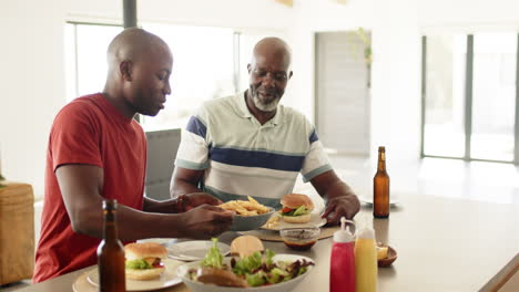 eating lunch together, african american father and adult son enjoying burgers and fries at home