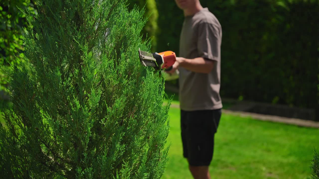 Uomo che pota una siepe verde con un tagliasiepi elettrico in giardino