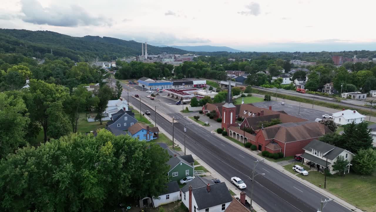 Traffic on road of American town with red brick church and historic single family Houses. Sunny summer day with green mountains in background. Aerial approaching shot. Waynesboro, Virginia
