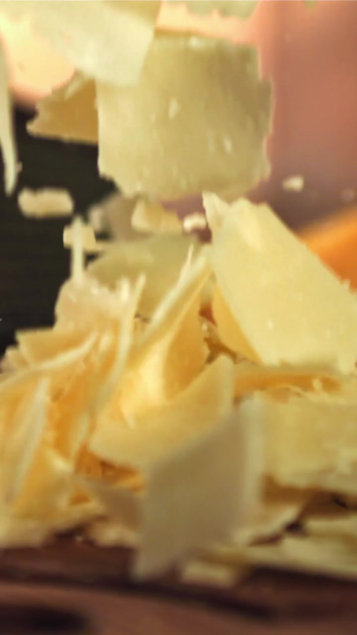 Scaglie di Parmigiano che cadono al rallentatore su una superficie di legno