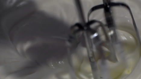 Up-close-macro-view-of-metal-mixer-stirring-and-spinning-delicious,-sweet,-white-icing-in-large-bowl-in-slow-motion