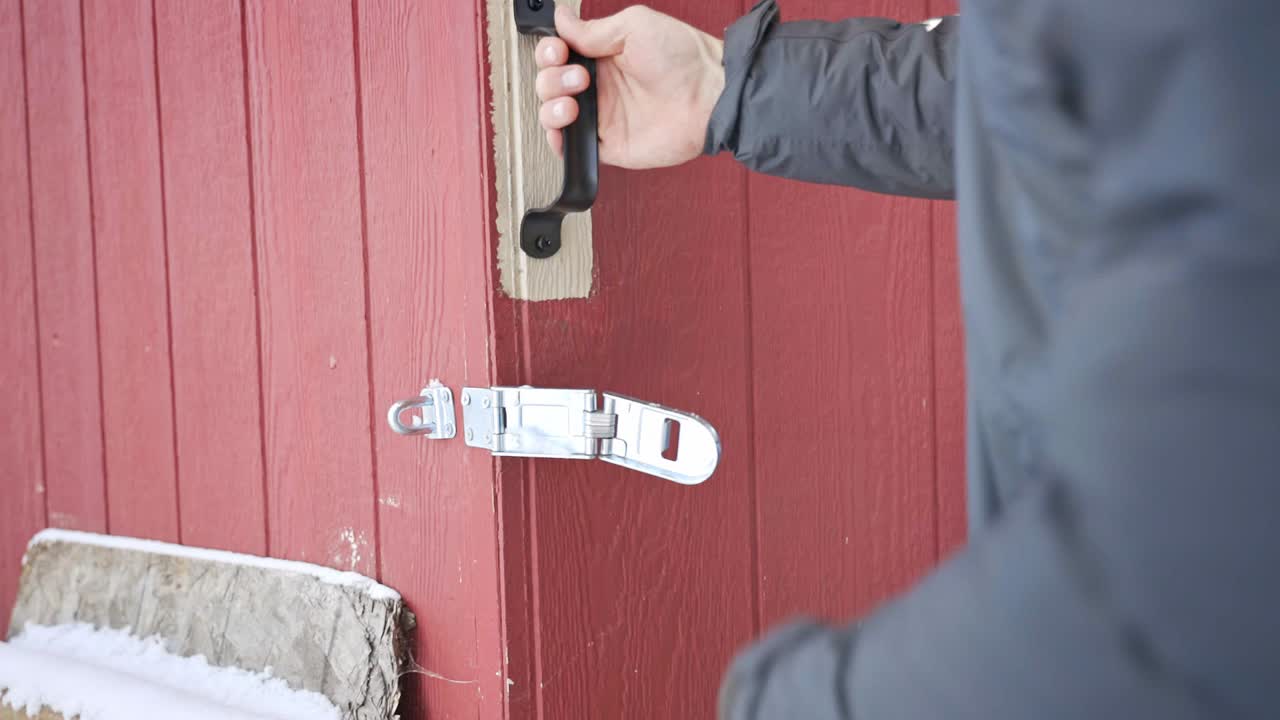 A man unlocks a clasp and slides open the door to a chicken coop during the winter