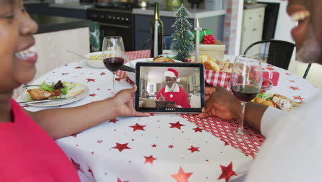 pareja afroamericana con vino usando tableta para la videollamada de navidad con santa en la pantalla