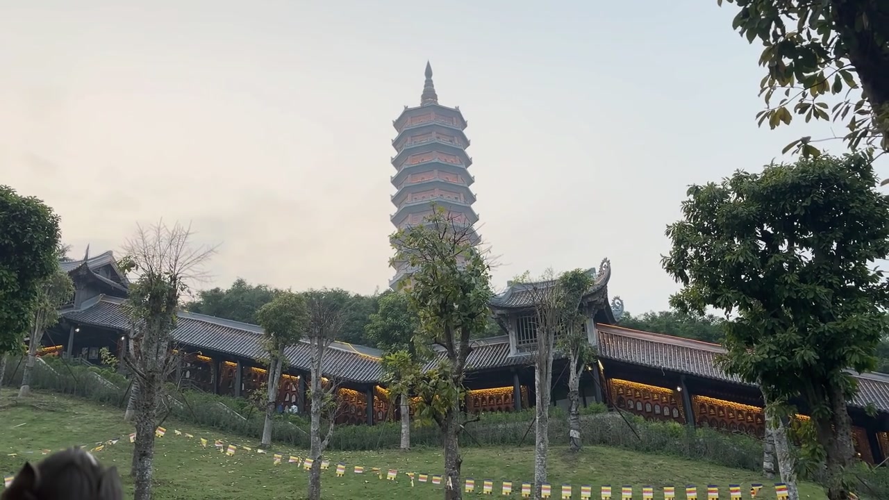 Soluk akşam gökyüzünün altında, kıvrımlı yamaç koridorlarının üzerinde yükselen Bao Thien stupasının yer aldığı, Vietnam'ın Ninh Binh şehrindeki Bai Dinh Pagodası'nın uzaktan görünümü.