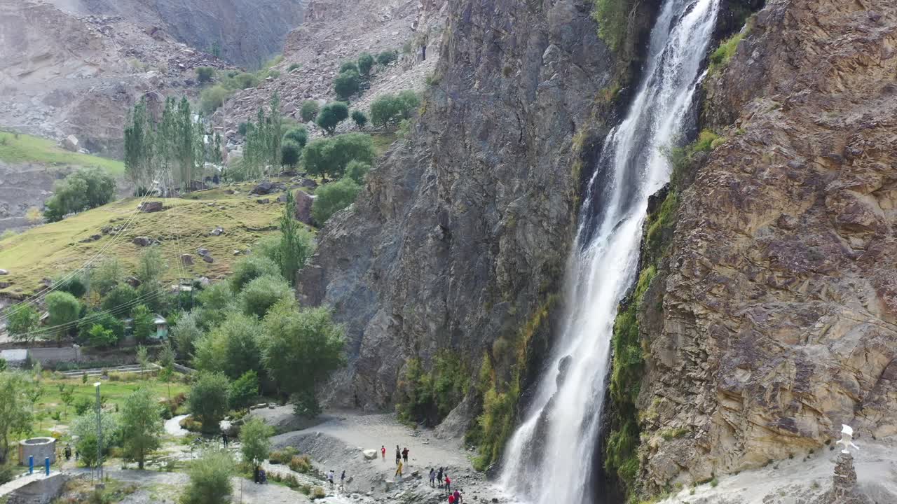 Drone aéreo panorâmico para a esquerda na Cachoeira Manthokha em Skardu, Paquistão, enquanto turistas abaixo são cercados por montanhas tirando fotos em um dia de verão ensolarado