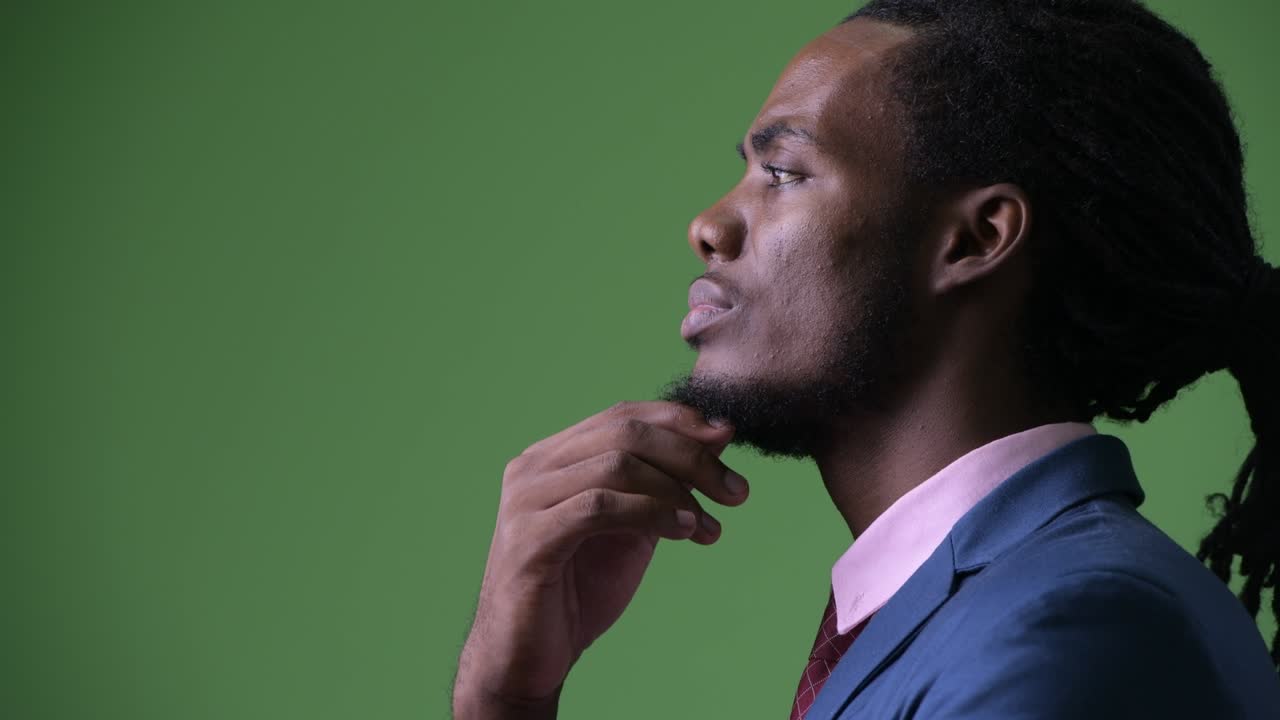 Young handsome African businessman with dreadlocks against green background