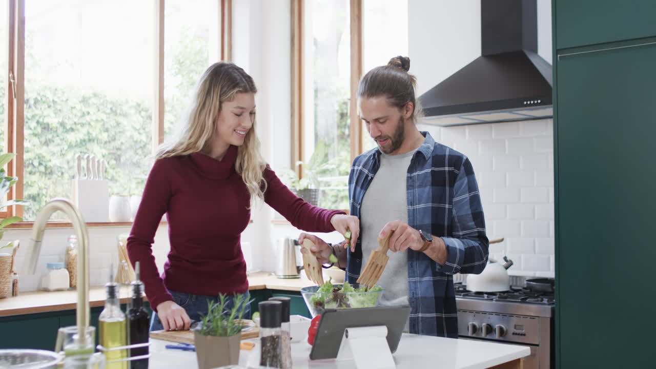 una pareja feliz preparando la cena en la cocina usando una tableta en casa, en cámara lenta