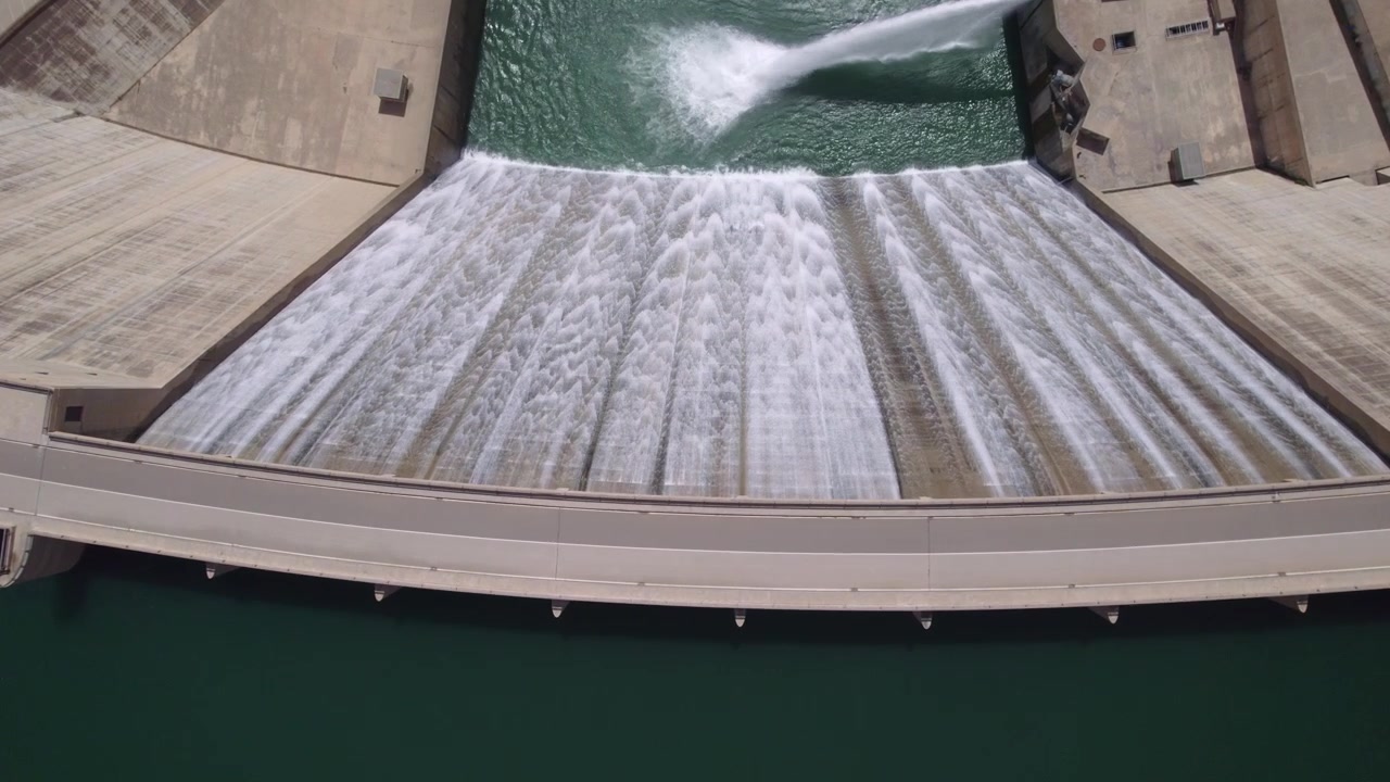 Presa en funcionamiento liberando agua, con la central hidroeléctrica descargando agua tras la generación por turbina. Vista aérea cenital durante el descenso. Central hidroeléctrica. Presa de Rules. España