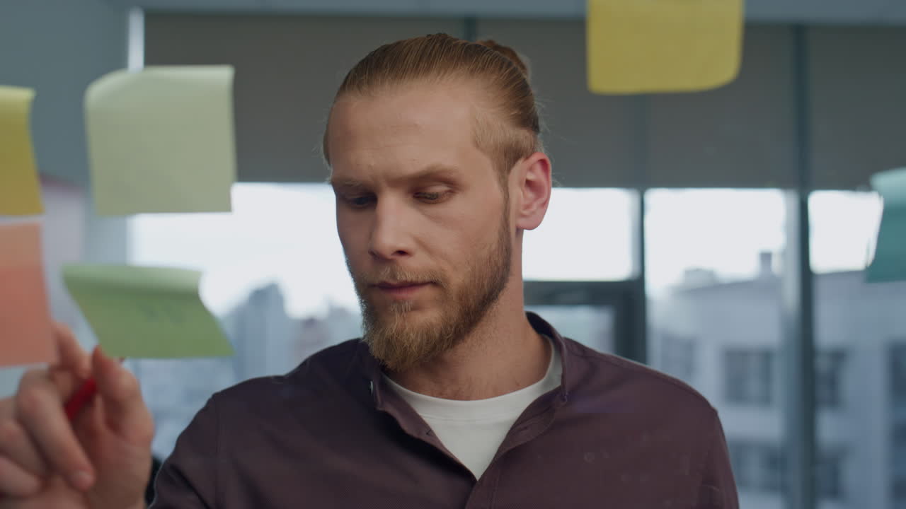 сосредоточенный менеджер ставит наклейку на прозрачную стену в офисе вблизи.