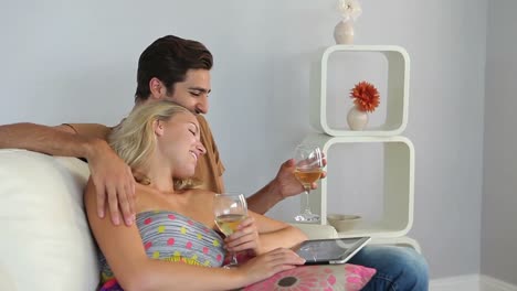 pareja sonriente acostada en el sofá usando una tableta pc bebiendo vino