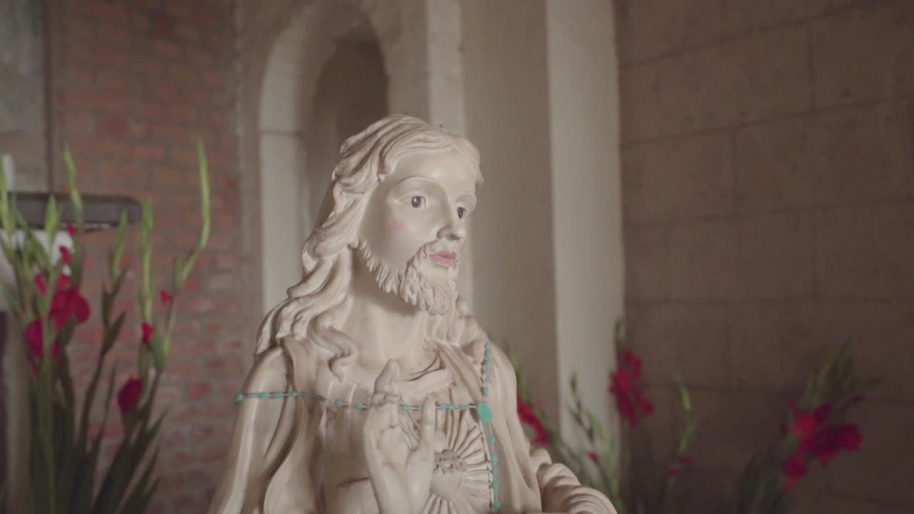 slow shot of a statue of Jesus Christ in an old church with a brick wall and candles