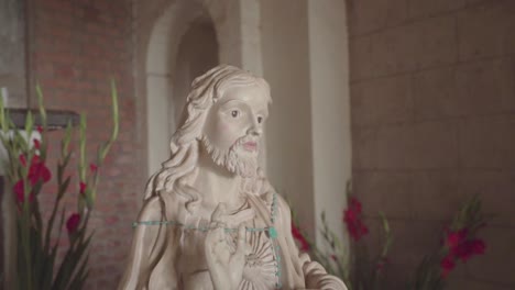 slow shot of a statue of jesus christ in an old church with a brick wall and candles