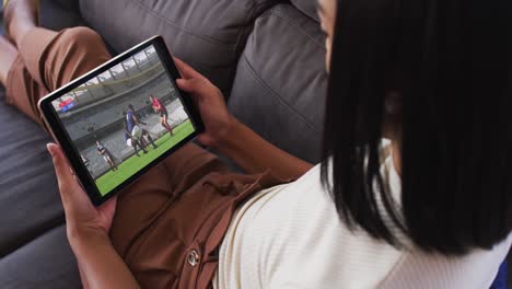 Zusammensetzung-Einer-Frau-Auf-Der-Couch-Zu-Hause,-Die-Sich-Ein-Rugbyspiel-Auf-Einem-Tablet-Ansieht