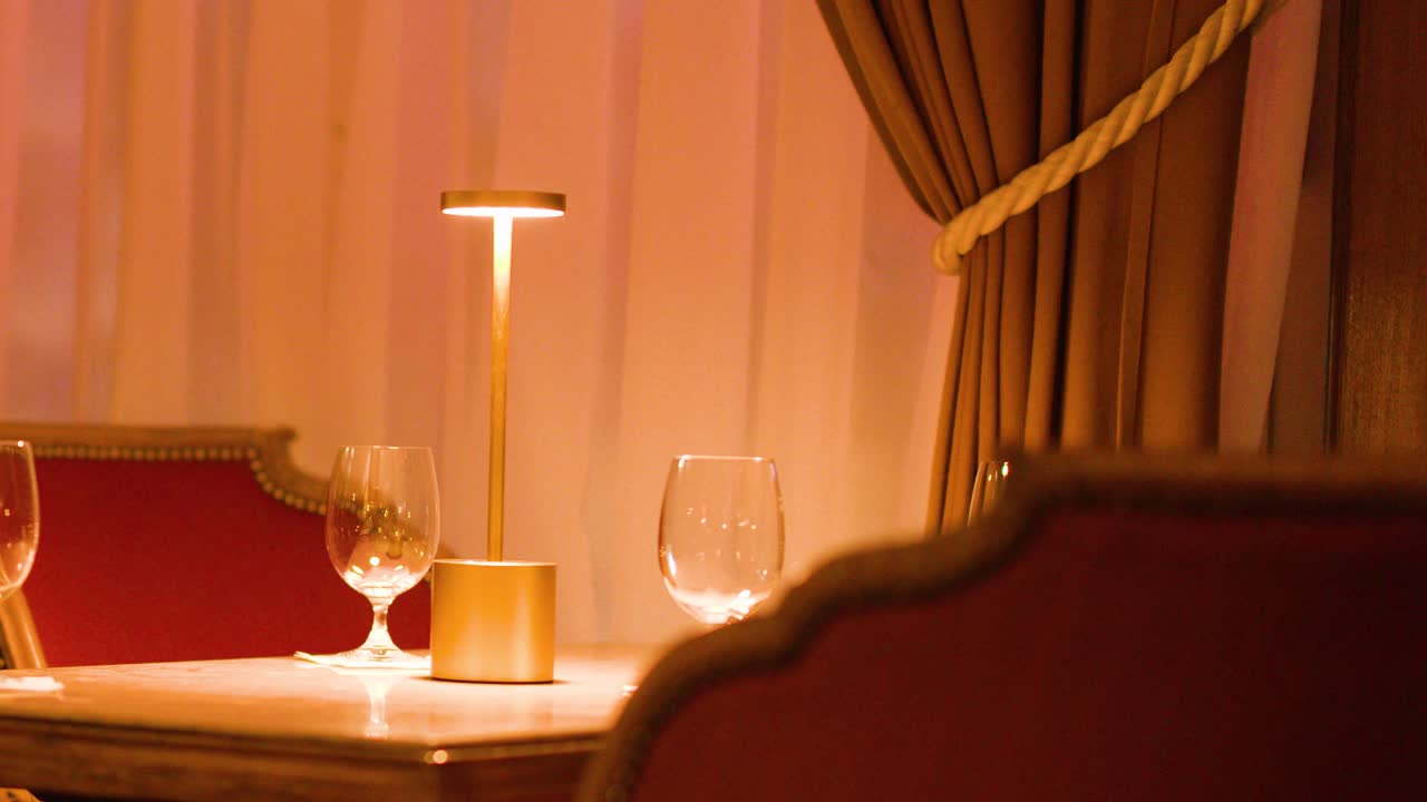 Luxurious restaurant interior with cozy seating, golden lamp, wine glasses, and intimate warm lighting