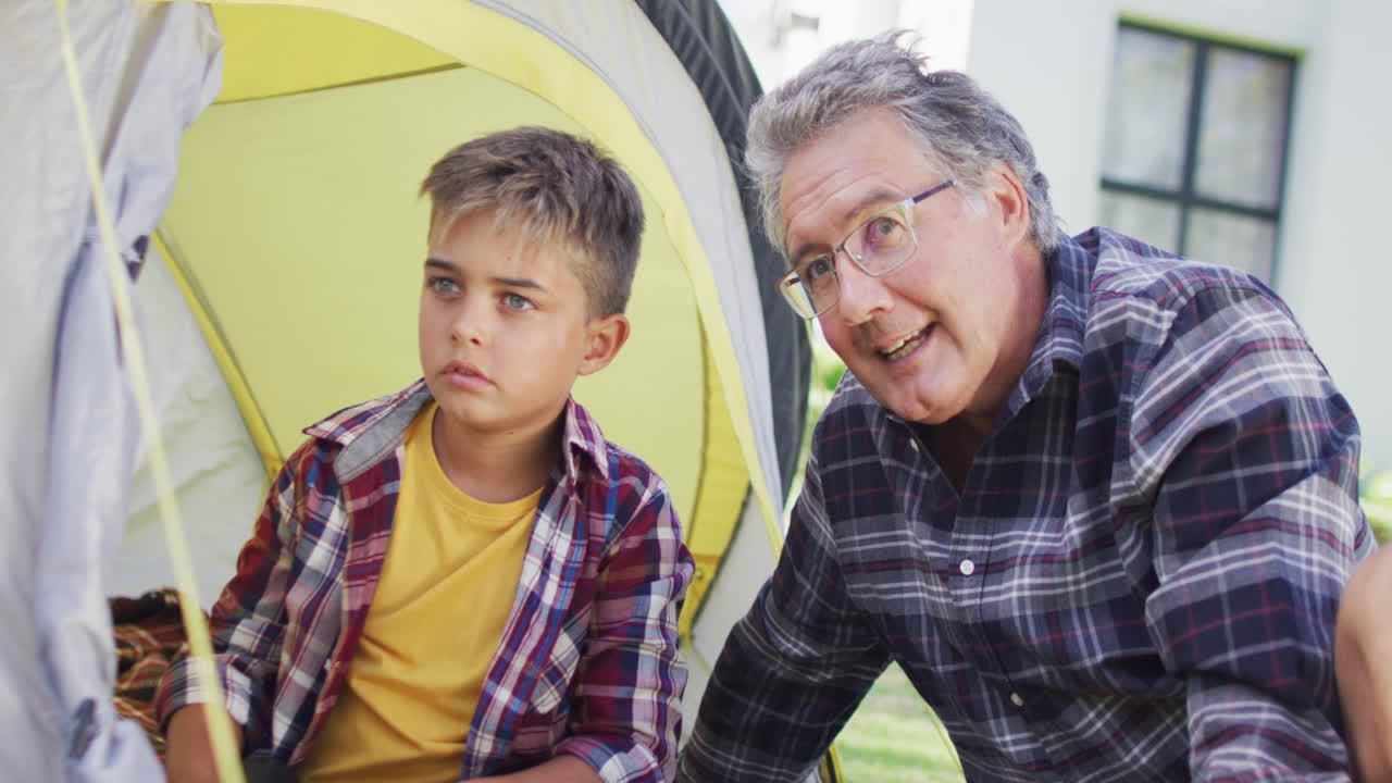Happy caucasian grandfather and grandson sitting in tent in garden, slow motion
