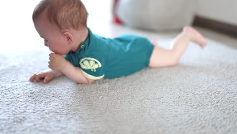 little baby boy rolling on the floor. cute kid opens mouth to put his fist and bangs the floor with a hand. blurred backdrop.