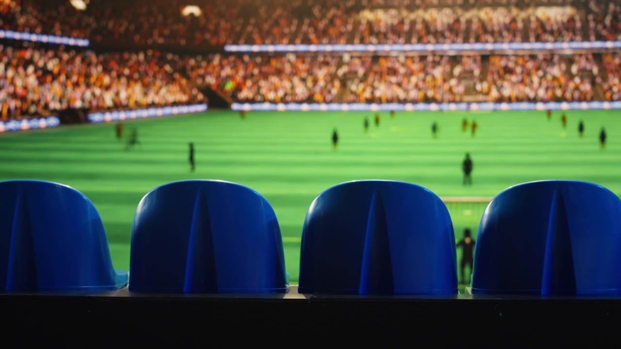 Close up of stadium seating facing blurred soccer field with players