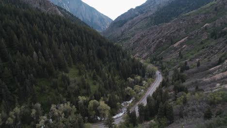 Panning-up-shot-of-canyon-road-in-Big-Cottonwood-Canyon,-Utah-with-a-vast-background-of-sunset-lit-mountains