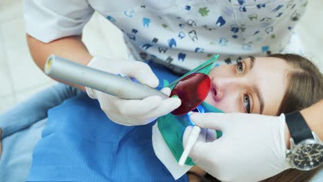 a dentist in white latex gloves uses a uv lamp with a red protective glass to solidify a dental filling. dental restoration and material polymerization with uv light