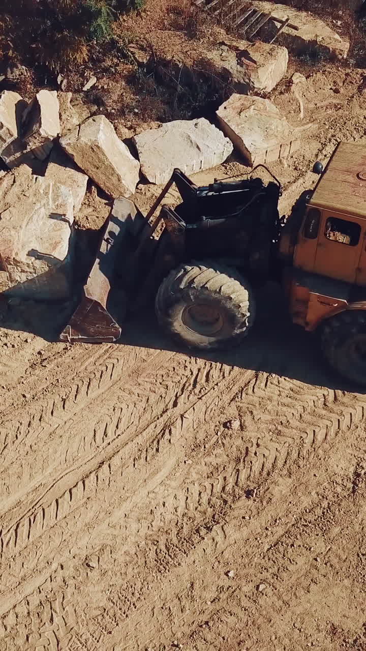 specially equipped bulldozer with a jug is picking up a stone in the quarry on the background of a rock with a forest. View of the sand quarry. Camera motion up.. Vertical video