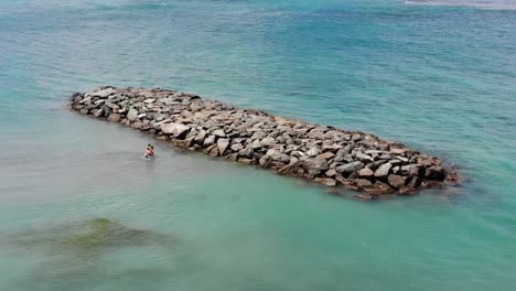 Aerial-footage-of-a-family-playing-in-the-beach-by-a-rock-formation