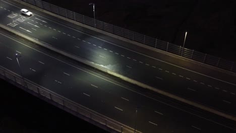 Vista-Aérea-Iluminada-Por-Encima-De-Los-Vehículos-Que-Conducen-Los-Carriles-De-Tráfico-De-La-Autopista-En-La-Noche-Pan-Izquierda-Inclinar-Hacia-Arriba