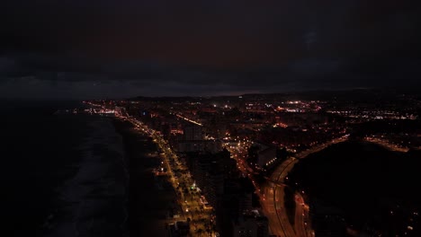 city lights illuminating the buildings and streets of torreblanca, spain, creating a mesmerizing nightscape as viewed from an aerial perspective by a drone, with the dark sea, drone pulling out