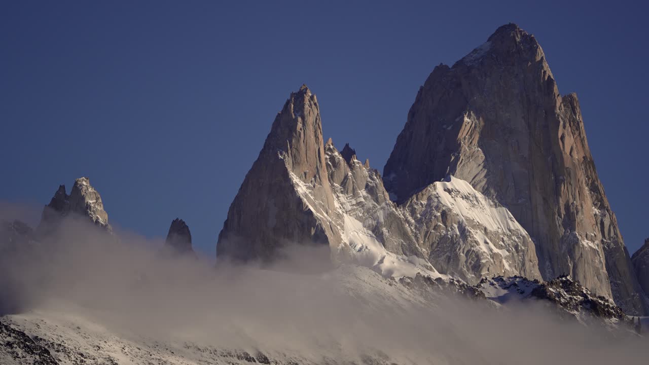 Time-lapse footage of Mount Fitz Roy and Aguja Poincenot in Patagonia, with low clouds drifting across the snowy peaks. Los Glaciares National Park.