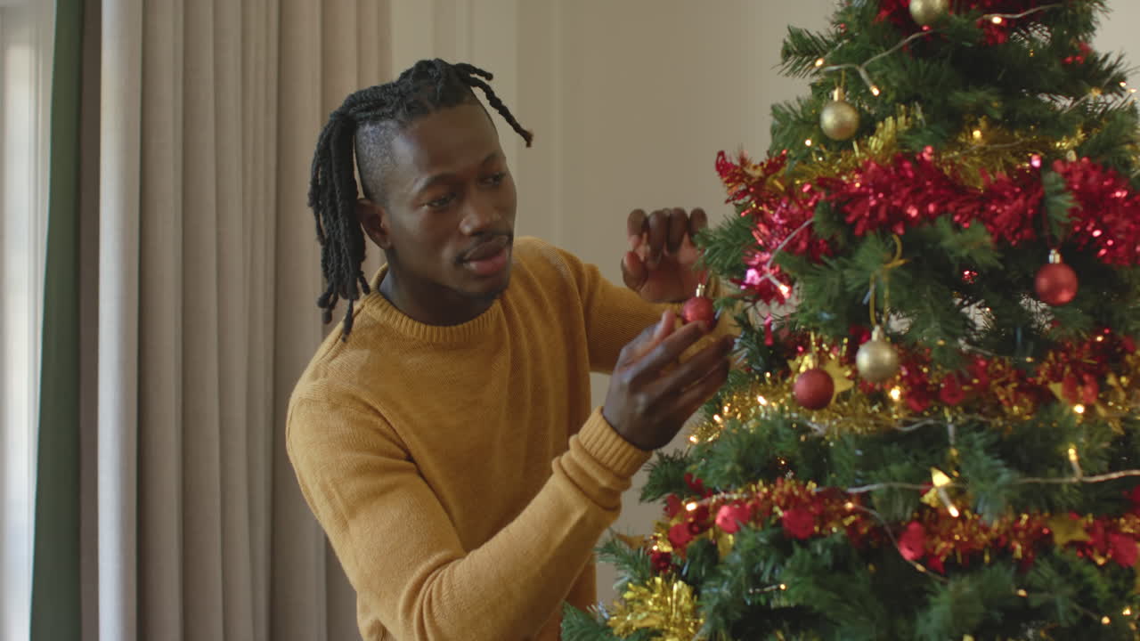 feliz hombre afroamericano con dreadlocks decorando el árbol de navidad, cámara lenta