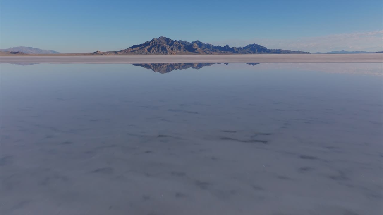 Drone flying at low altitude over water surface of flooded Bonneville Salt Flats with rocky mountain in background, Utah