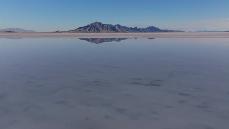 drone flying at low altitude over water surface of flooded bonneville salt flats with rocky mountain in background, utah