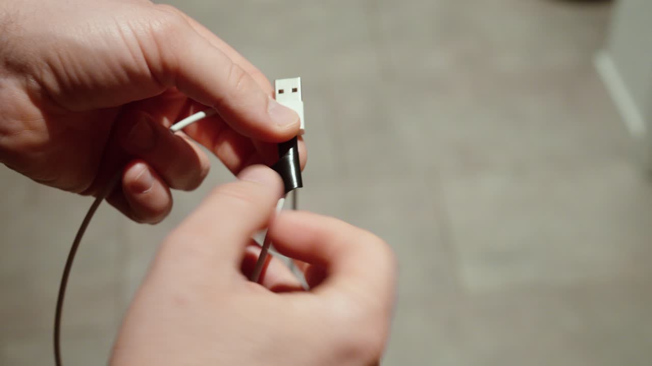 Close-up of hands showing a damaged charging cable with broken insulation. Concept of electrical safety, faulty electronics, cable wear, and device charging problems