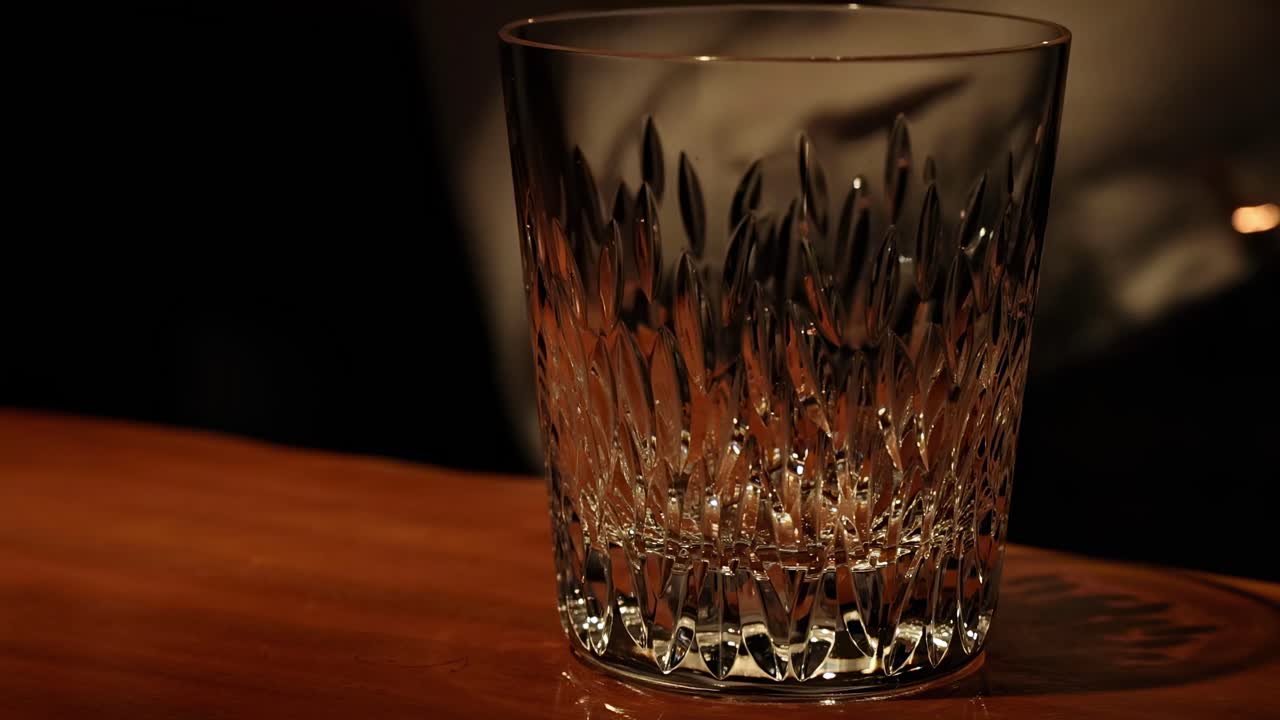 A detailed crystal glass sits on a warmly lit wooden surface, showcasing intricate patterns.
