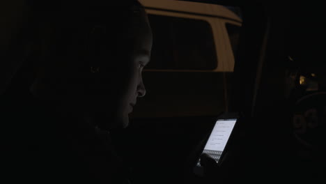 young woman using cellphone during night car ride in the city